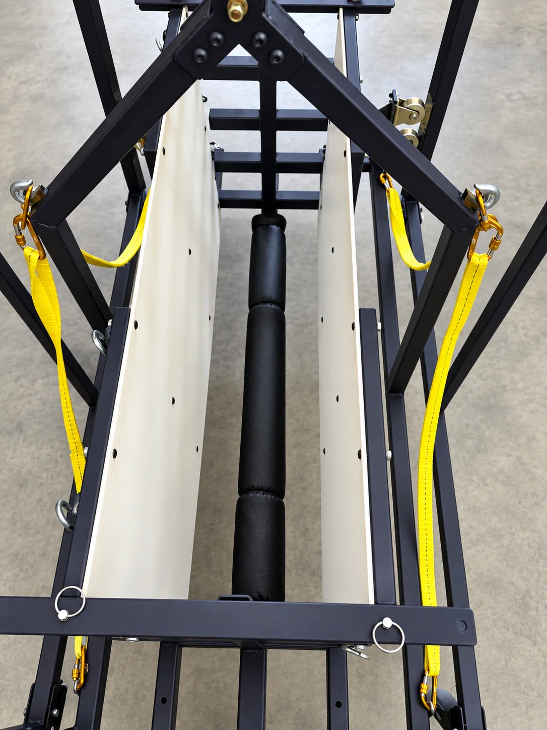 Top-down view into the chute of the Juniper Pig Lift, showing the heavily padded central bar between two smooth side panels with yellow webbing at each corner.