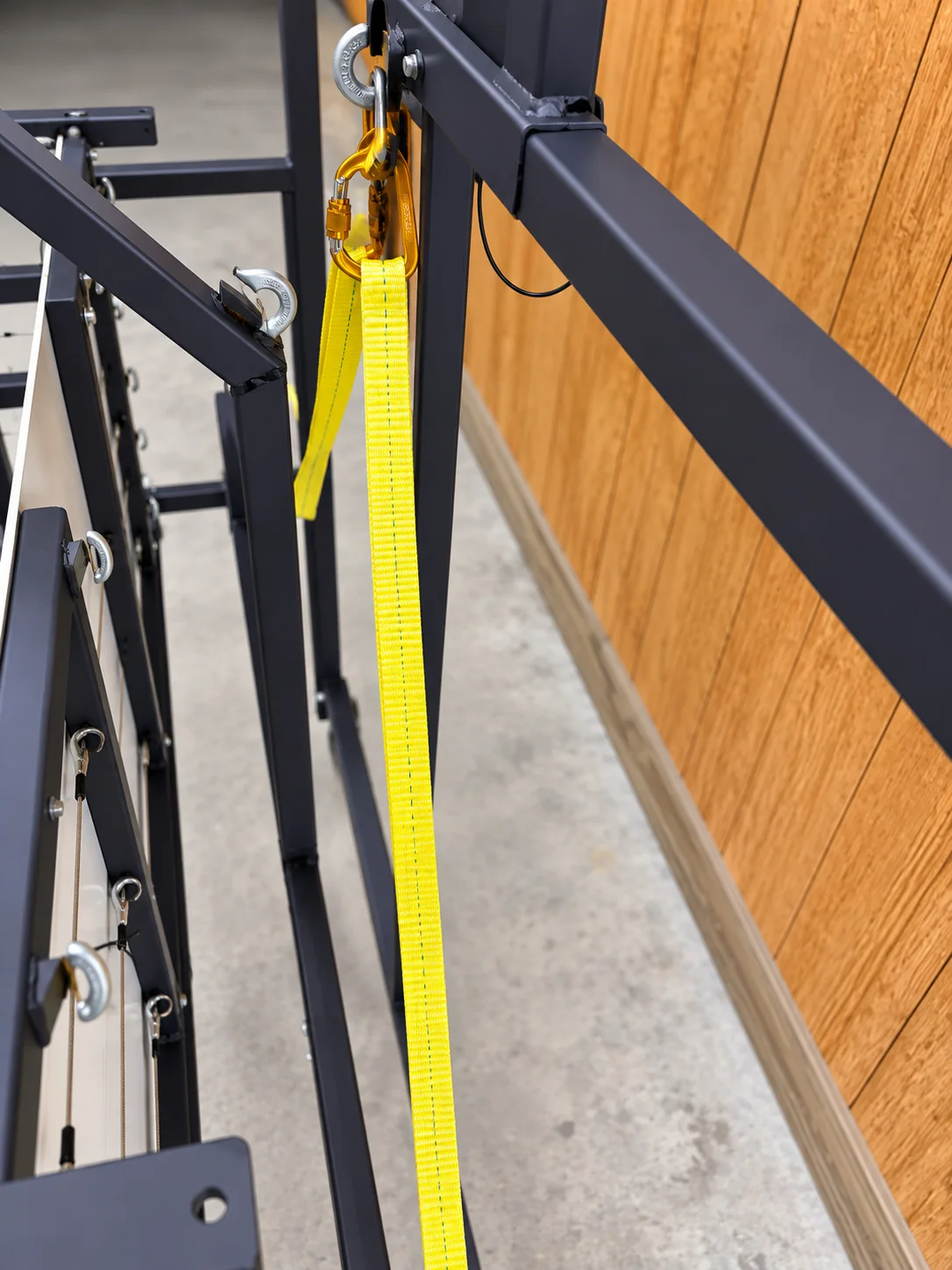 Close-up of yellow safety webbing clipped to the frame with a carabiner through an eye bolt.