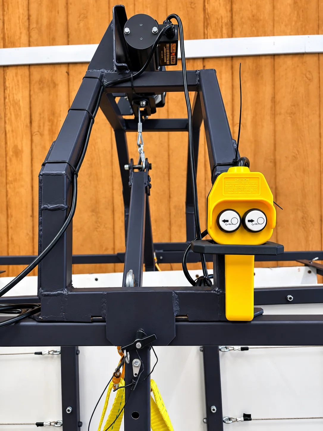 Close-up of the winch motor at the top of the frame and the yellow two-button pendant control resting on its bracket.